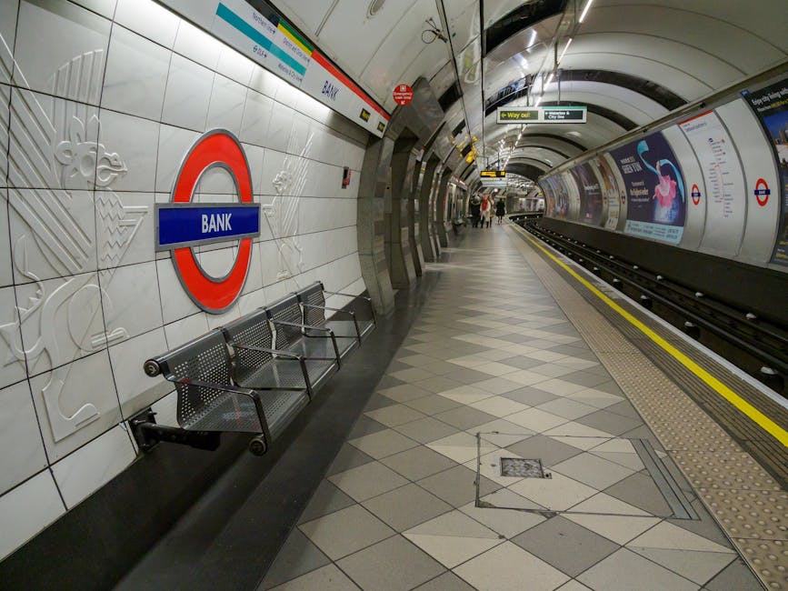 A photograph taken at an underground London Tube station shows a clean, modern platform with white tiled walls featuring embossed floral patterns and a prominent red and blue London Underground 'Bank'